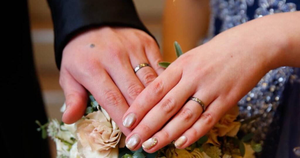 タンタル製の結婚指輪を着けた新郎新婦の手、ブーケを持って重ね合わせている様子