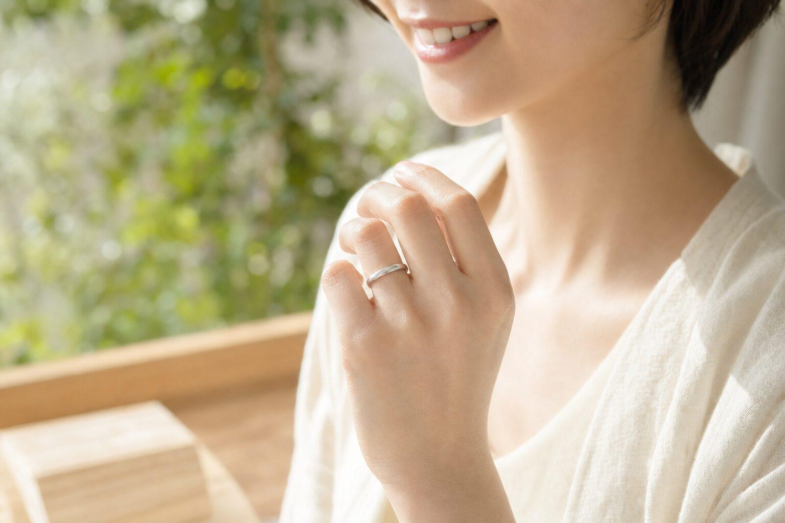 明るい窓辺で金属色の指輪を着けた女性の手元