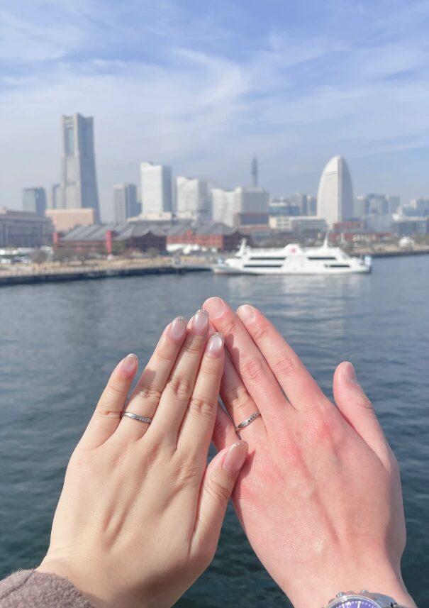 港を背景に結婚指輪を着けたお二人の手元