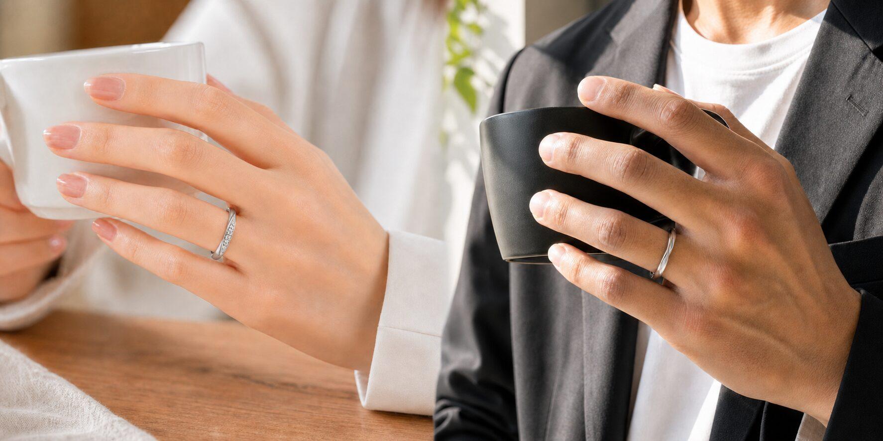 細身の結婚指輪を着けてマグカップを持つ二人の手元